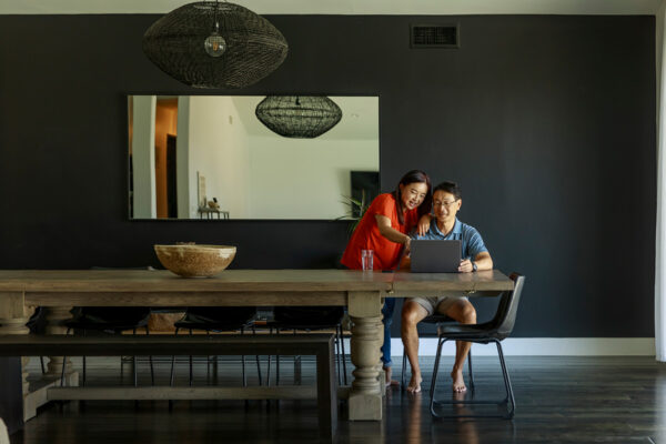 Asian man and woman in large dining room looking at laptop to determine which of the AAO Endorsed Insurance Program's Life Insurance is best for them.